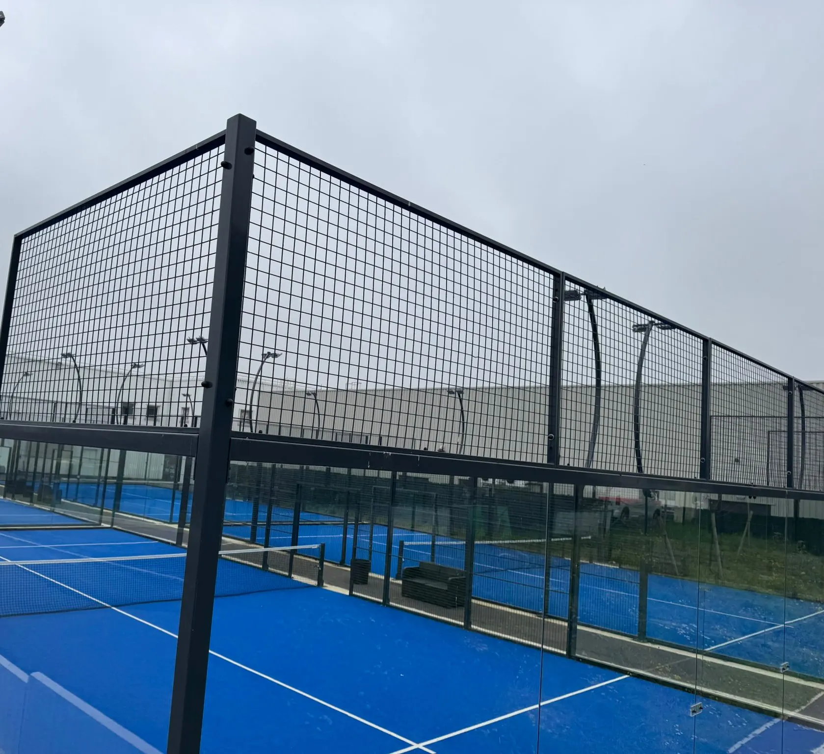 Temperli cam panelleri ve tel örgüsüyle kapatılmış açık padel kortu